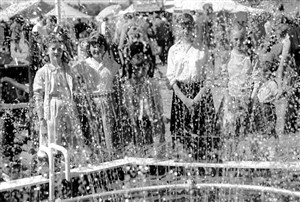Photo:Children seen through the spray of a fountain.